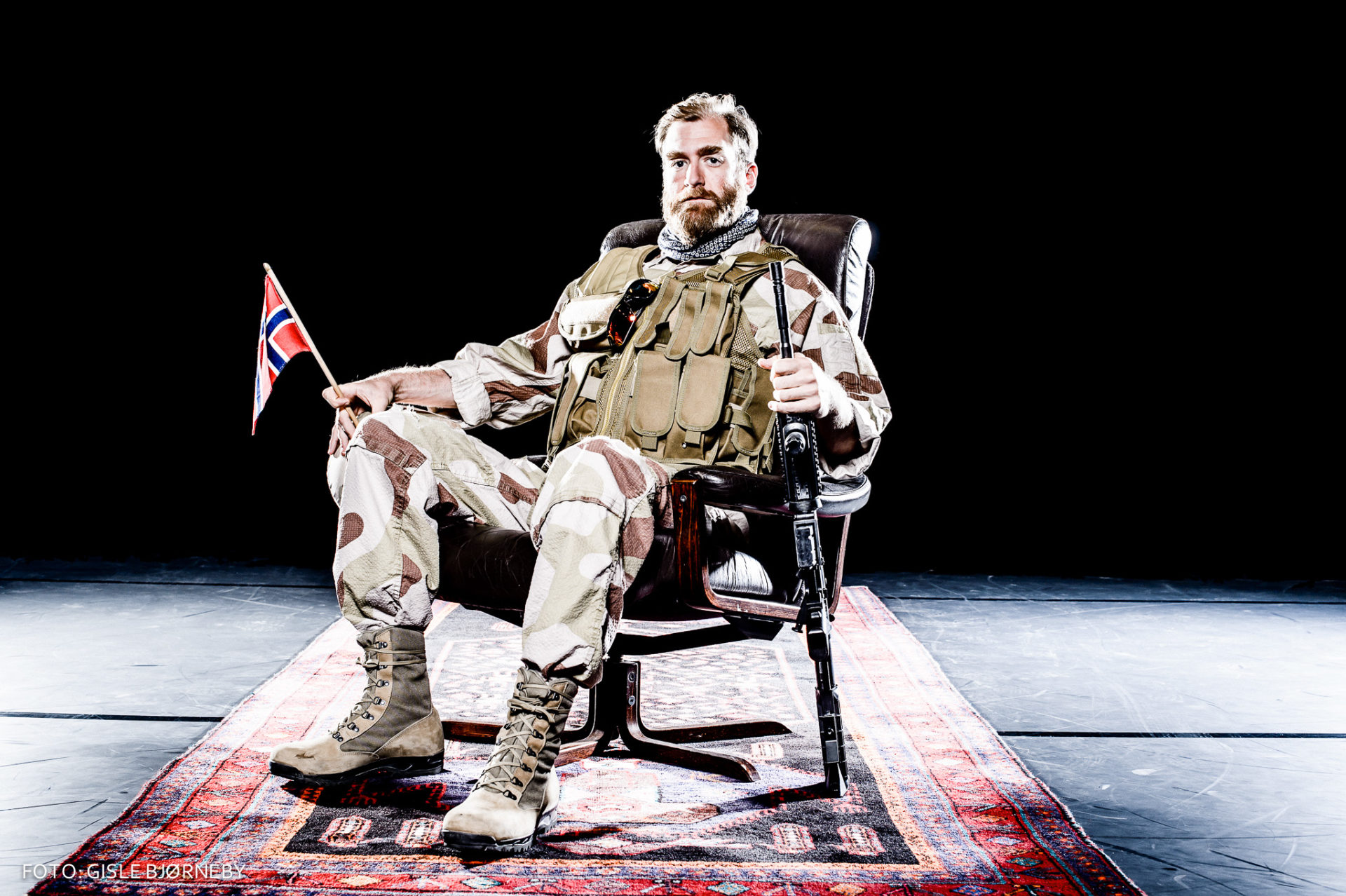 mann i militærklær med gevær og flagg sitter i stol