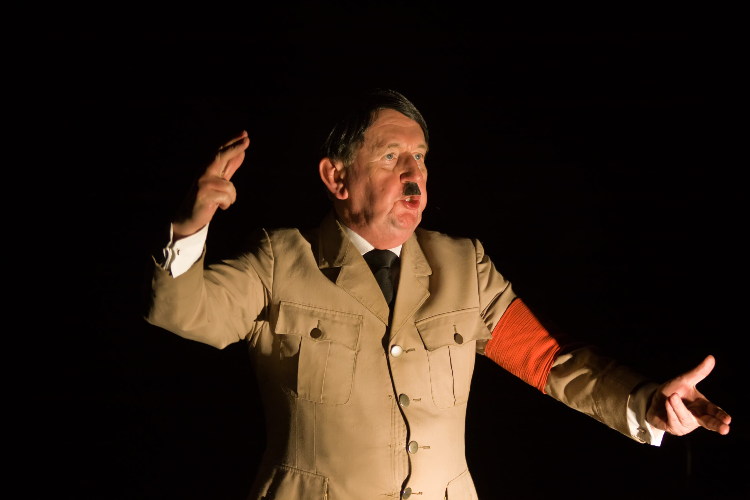 Skuespiller i Adolf Hitler-kostyme og sminke/bart holder tale med gestikulerende armer.