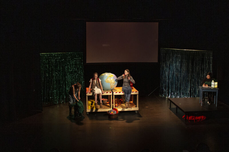 Fire ungdommer på scenen. To sitter på et bord med en stor badeball-globus.