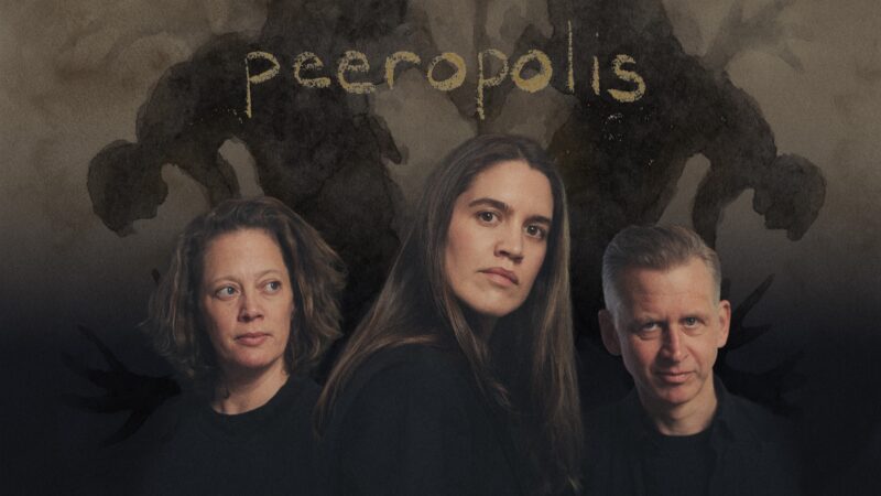 En kvinne står foran en annen kvinne og en mann. De står bak, på hver sin side av kvinnen i front