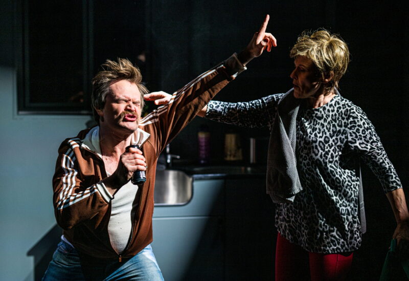 En mann rocke-danser med en brusboks som mikrofon. En kvinne er i ferd med å ta på skulderen hans.