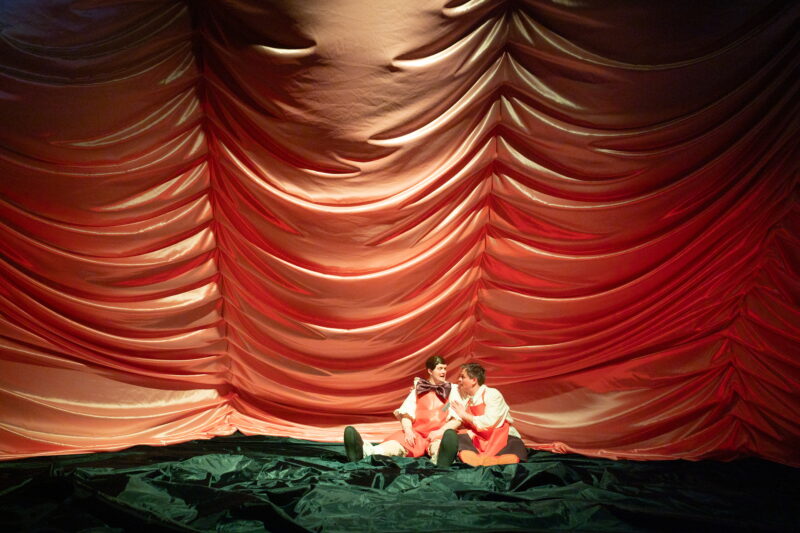 To personer, Pinocchio og Gepetto, sitter ved siden av hverandre på et grønt teppe.